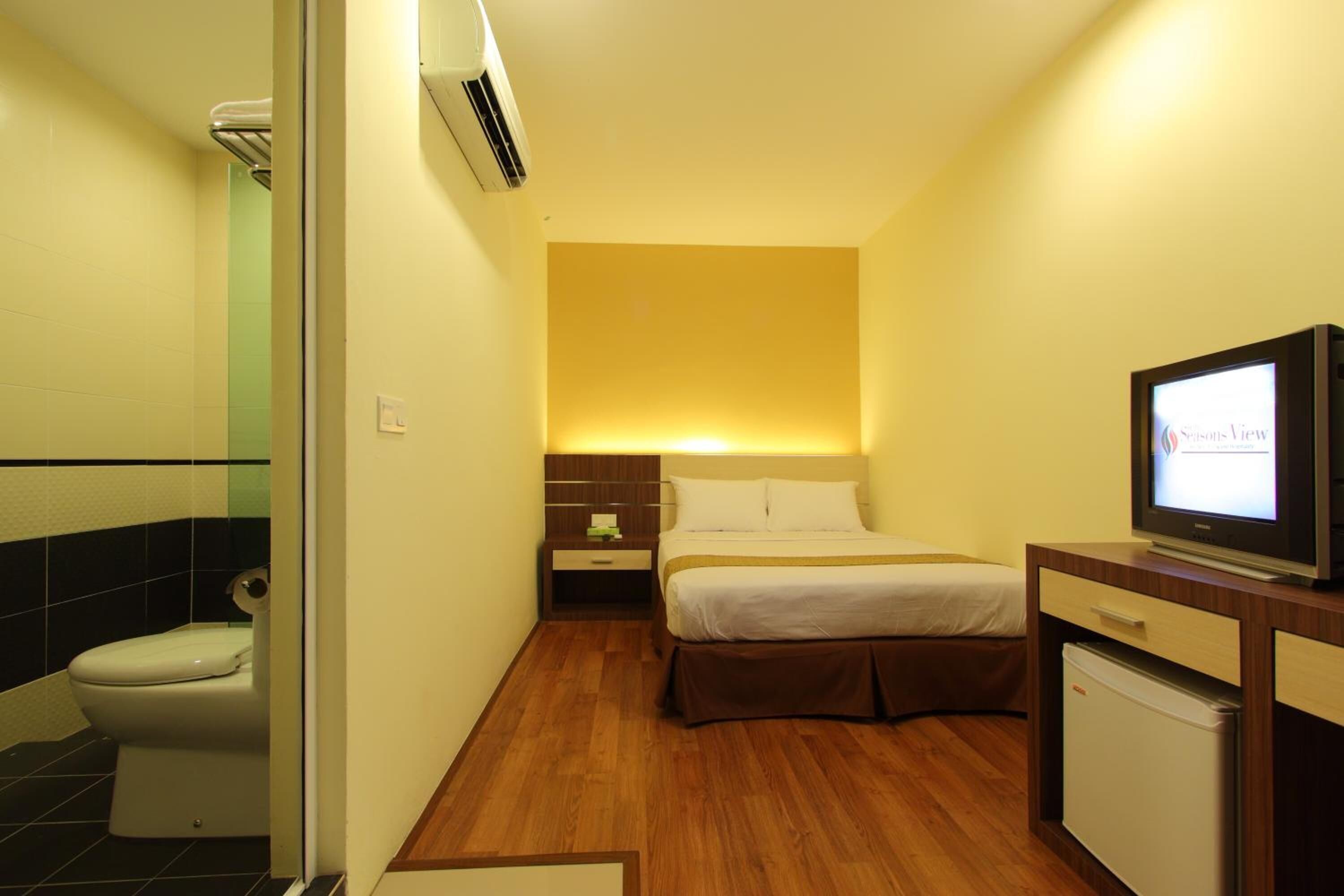 A compact hotel room with a bed, bedside table, TV, and a small refrigerator.