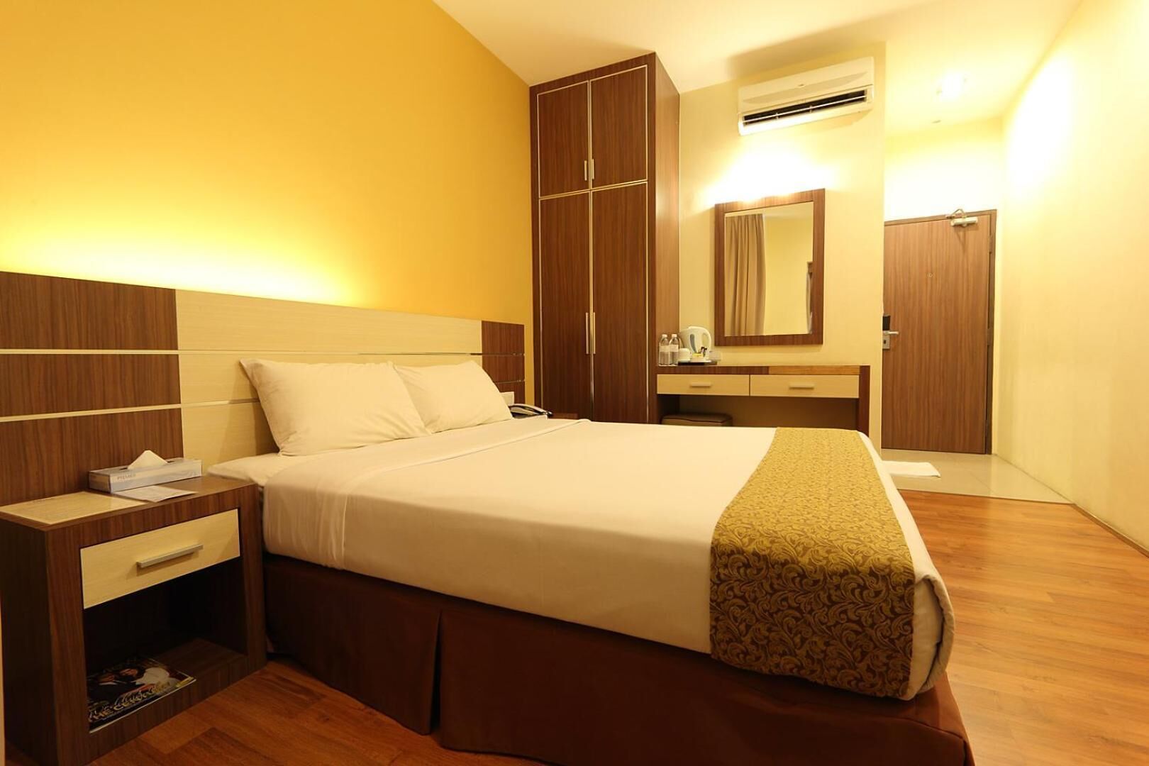 Habitación de hotel con cama, mesita de noche, cómoda, espejo y equipo de aire acondicionado.