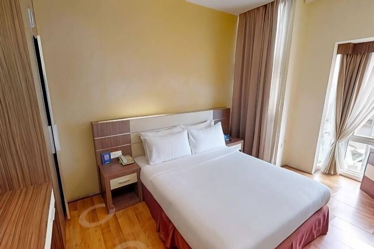 A hotel room with a bed, bedside table, and curtains.