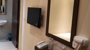 Une chambre d’hôtel dotée d’un grand miroir, d’un téléviseur fixé au mur, d’un téléphone sur la table de chevet, d’un sèche-cheveux et d’une petite table avec un carnet et des bouteilles d’eau.