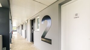 Un pasillo con un gran número 2 en la pared, que indica el número de habitación. Hay puertas a la derecha y un cartel en la pared que dice 'Lingerie'.