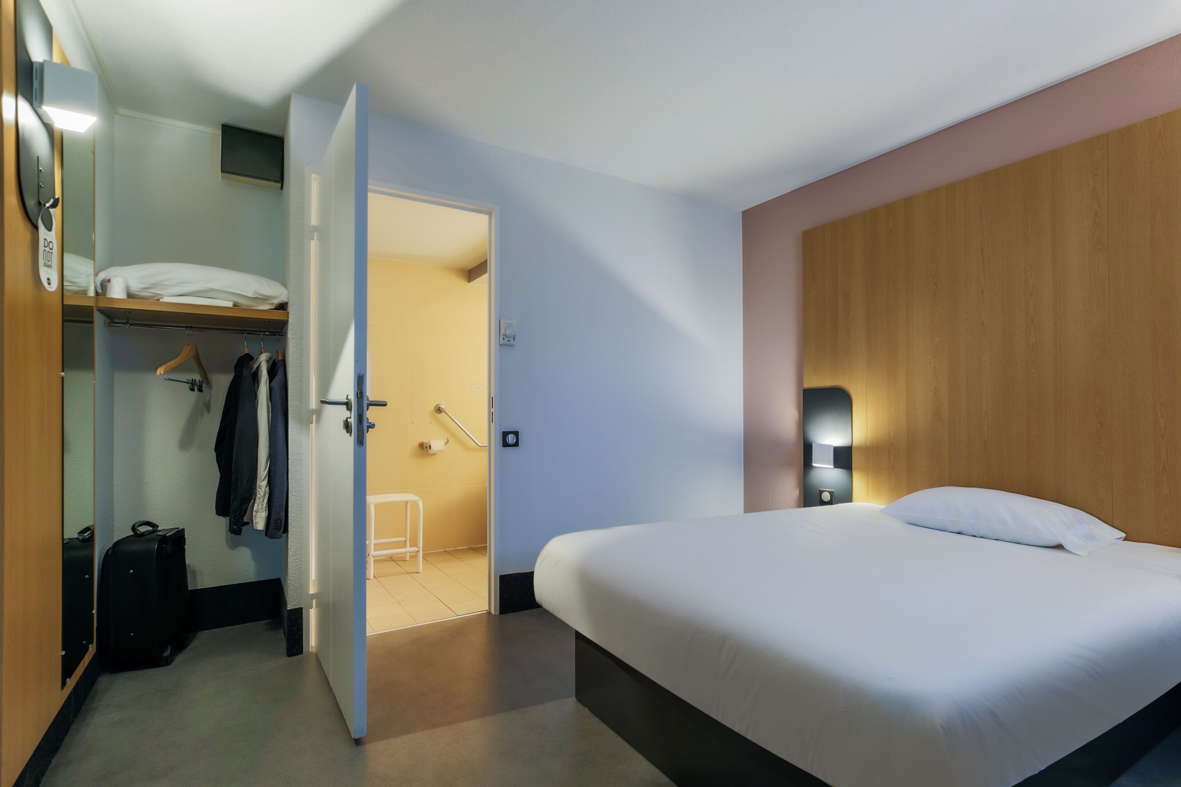 Una habitación de hotel con cama, armario, espejo y puerta que da a un baño.