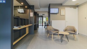 Zona de recepción con escritorio, sillas, televisor montado en la pared y tablón informativo.