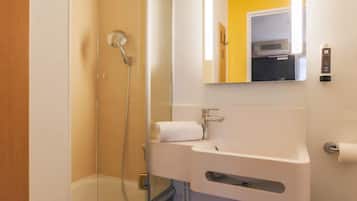 Une salle de bain moderne avec une douche à l’italienne en verre, un lavabo blanc avec une serviette, et un miroir qui reflète un mur jaune et une porte.