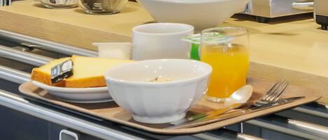 A breakfast tray with a bowl of cereal, a glass of orange juice, a plate with a slice of cake, and a cup.