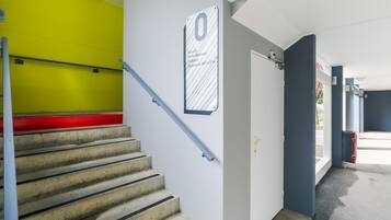 Una escalera con barandilla metálica, un letrero que indica el número de habitación cero y una puerta que da a una habitación.