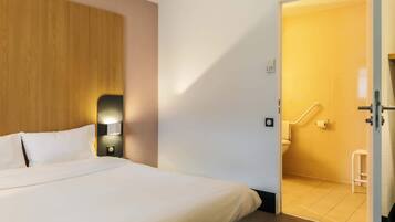 Camera d'albergo con un letto, un comodino, una lampada a parete e un bagno visibile attraverso una porta aperta.