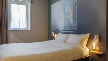 A neatly made bed with white linens, a window with curtains, and wall-mounted bedside lamps.