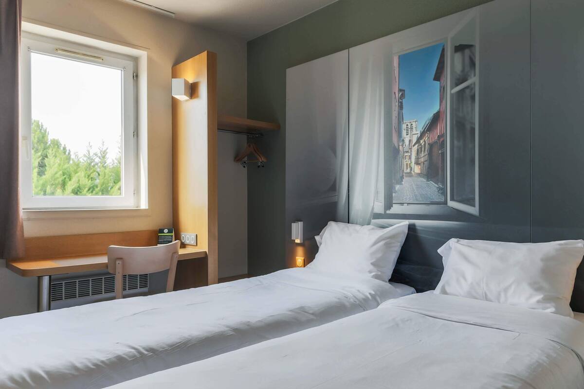 Ein Hotelzimmer mit Bett, Schreibtisch und Fenster mit Blick auf Gebäude.