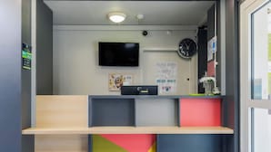 A reception area with a flat-screen TV, a clock, and a bulletin board. - B&B HOTEL Metz Jouy-aux-Arches (Jouy-aux-Arches)