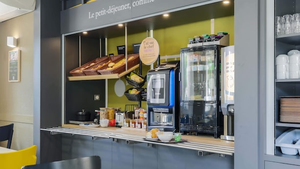 A breakfast bar with a display of pastries, a coffee machine, and a sign that reads "Le petit-déjeuner, comme chez vous". - B&B HOTEL Metz Jouy-aux-Arches (Jouy-aux-Arches)