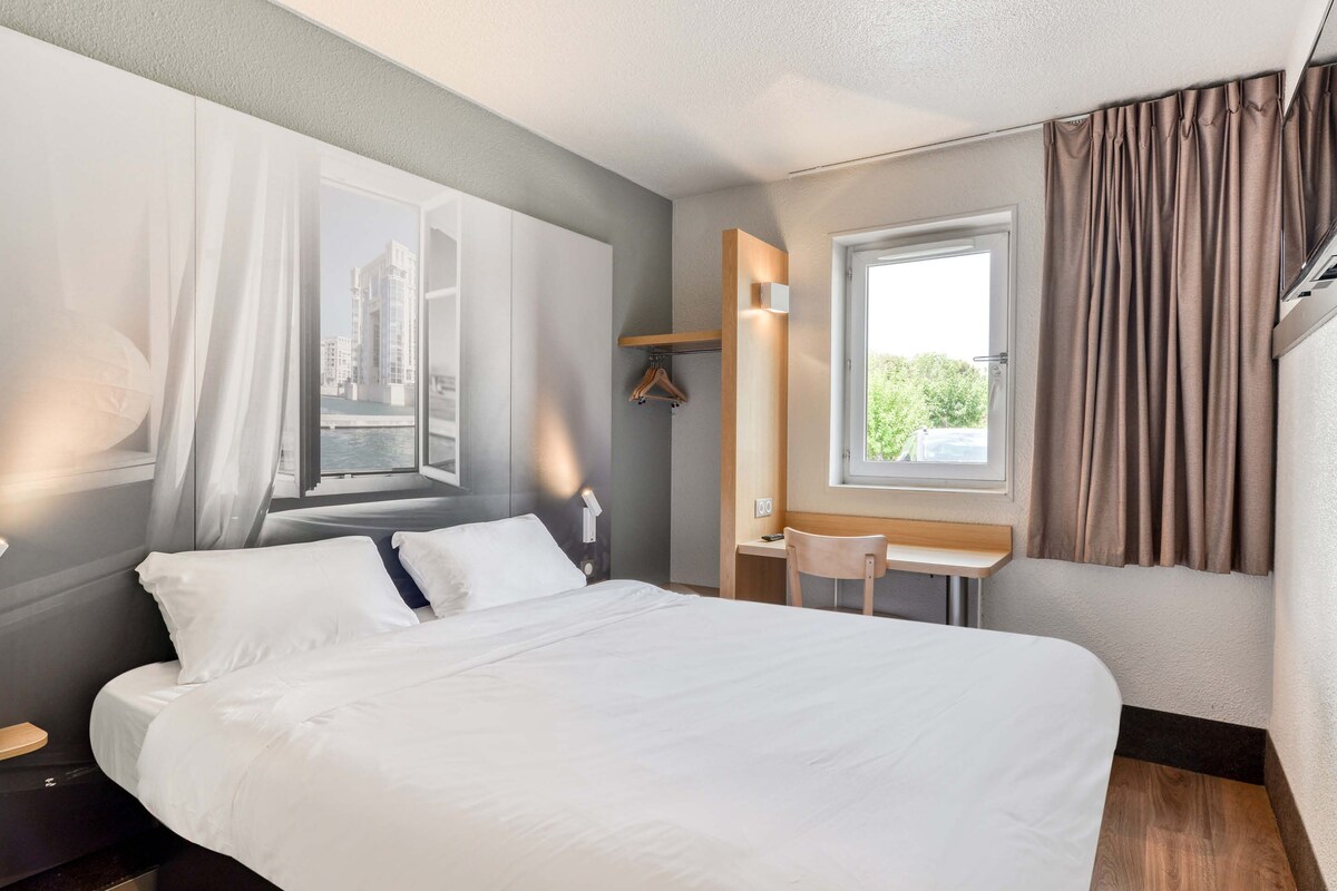 A modern hotel room with a large bed, a desk, and a window with curtains.