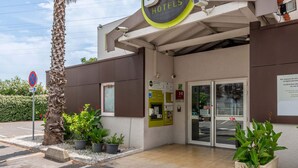 A B&B hotel entrance with a palm tree, potted plants, and a signboard. - B&B HOTEL Montpellier (1) (Saint-Jean-de-Vedas)