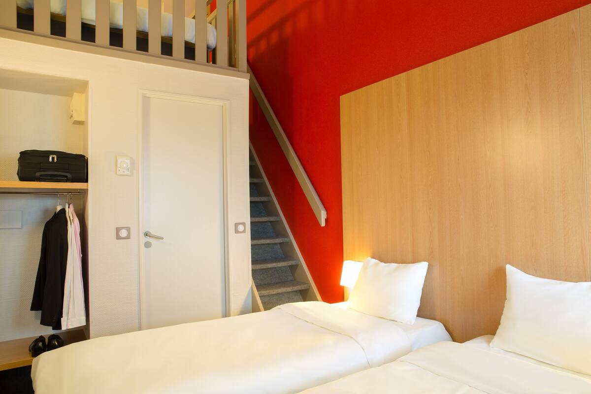 Een hotelkamer met een bed, een kledingkast met daarin hangende kleding en een trap.