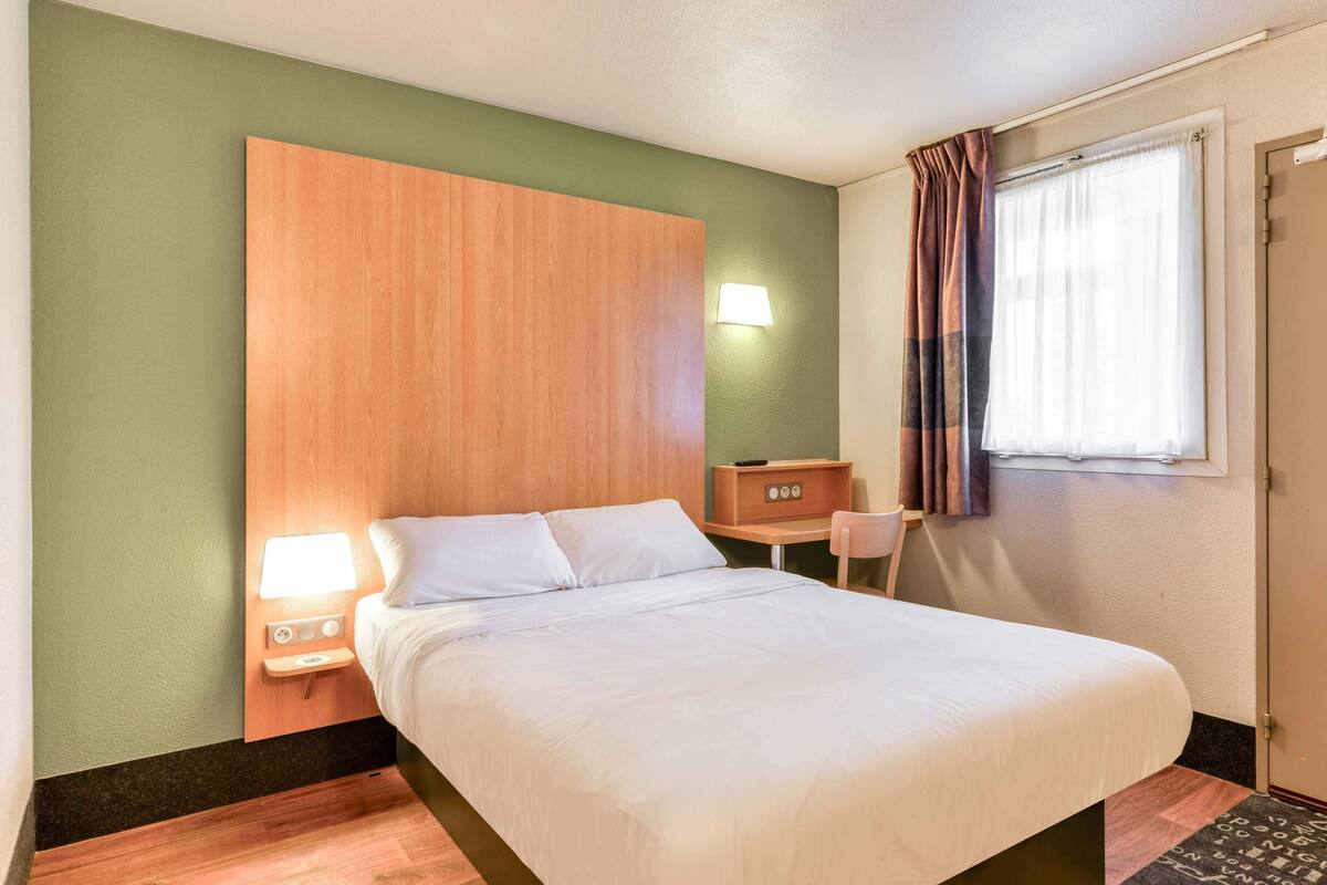 Een hotelkamer met een bed, nachtkastje met lamp, bureau en stoel.