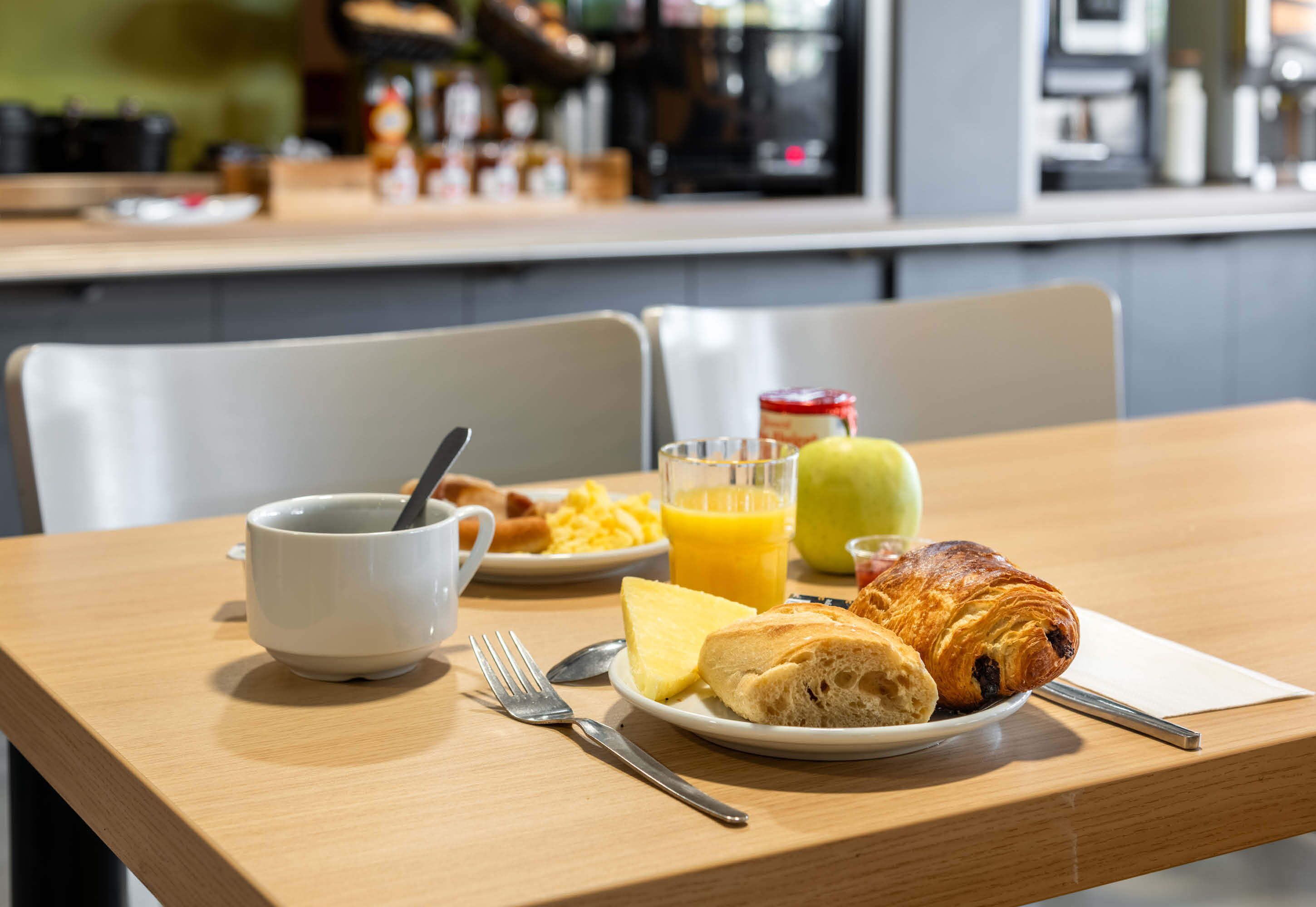 Ein Frühstückstisch mit einem Croissant, einem Glas Orangensaft, einer Schüssel Müsli und einer Tasse Kaffee.