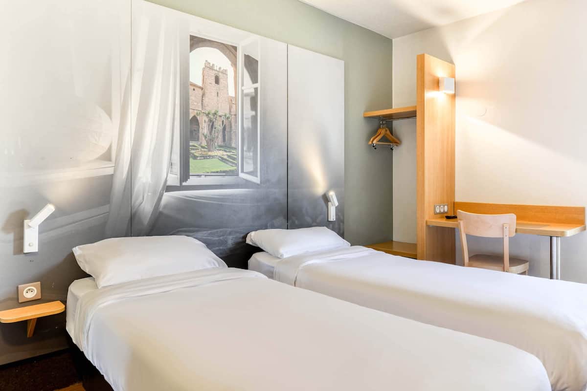 Une chambre d’hôtel avec deux lits, un bureau et une vue sur un château, visible par la fenêtre.