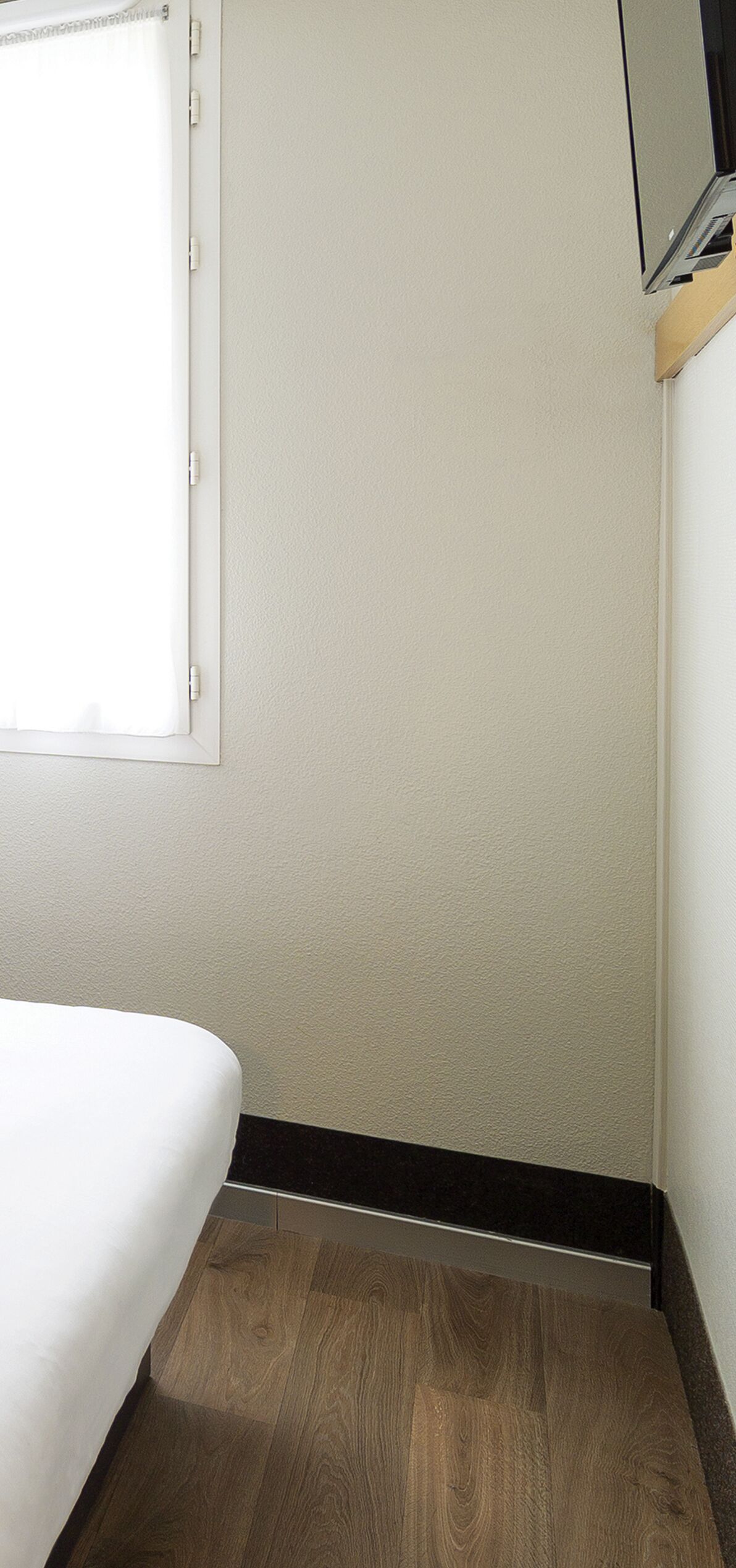 Una habitación con una cama, una ventana con persianas, suelo de madera y un televisor montado en la pared.