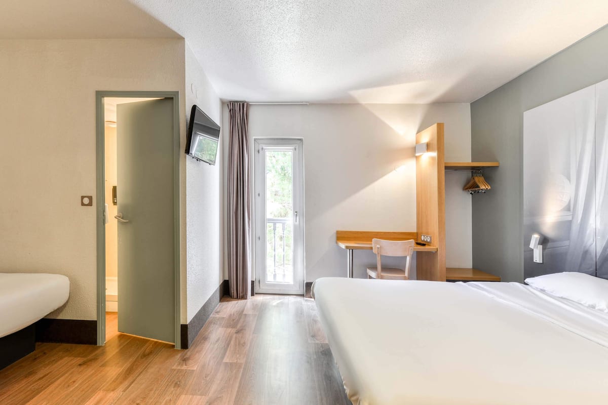 Une chambre d’hôtel équipée d’un lit, d’un bureau, d’une chaise, d’une télévision et d’une porte donnant sur un balcon.