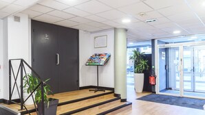 Un lobby moderno con una escalera, un extintor, un cartel de bienvenida y una puerta que da al exterior.