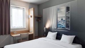 Hotelkamer met een bed, bureau, stoel, raam met gordijnen en een wandlamp.