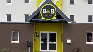 Een B&B hotel met een opvallende geel-bruine gevel, een herkenbaar logo en een paar dubbele deuren.