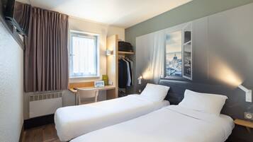 Une chambre d’hôtel avec deux lits, un bureau, une chaise, un porte-manteau et une fenêtre avec des rideaux.