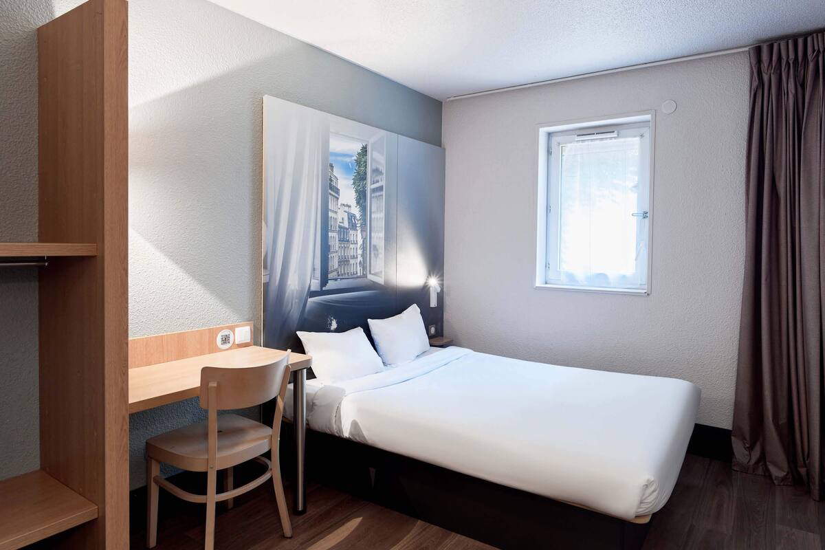 A hotel room with a bed, a desk, a chair, and a window with curtains.