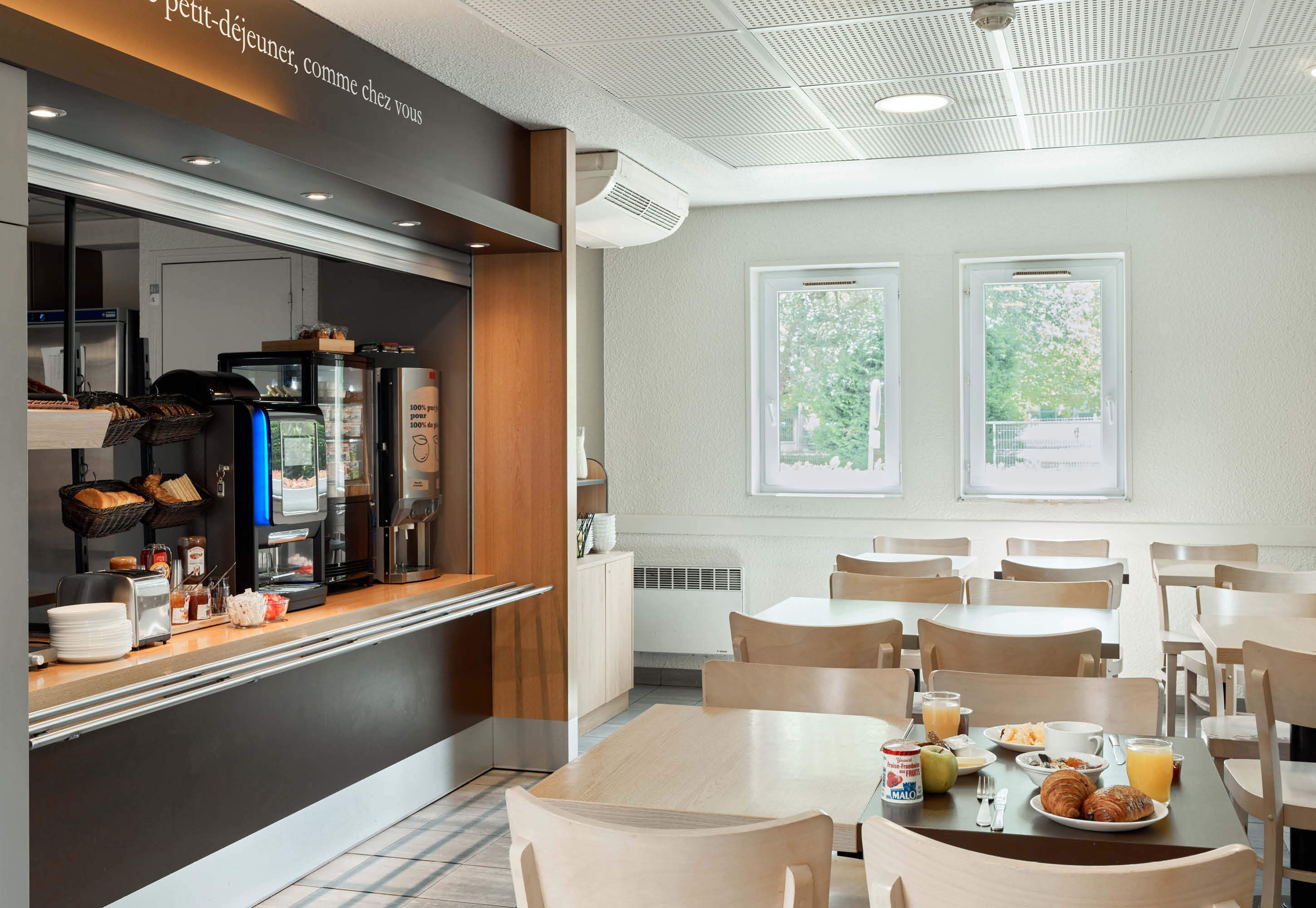 Un espace moderne dédié au petit-déjeuner, doté d’un comptoir en libre-service, de différents types de sièges et de grandes fenêtres laissant entrer la lumière naturelle.