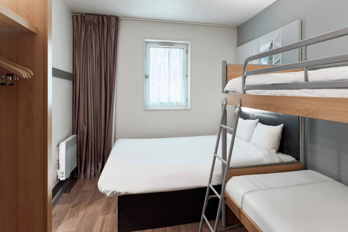 A compact room with bunk beds, a window with curtains, a radiator, and a wooden floor.