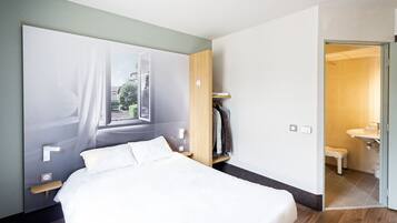 Una habitación de hotel moderna con una cama grande, un armario y un baño visible a través de una puerta abierta.