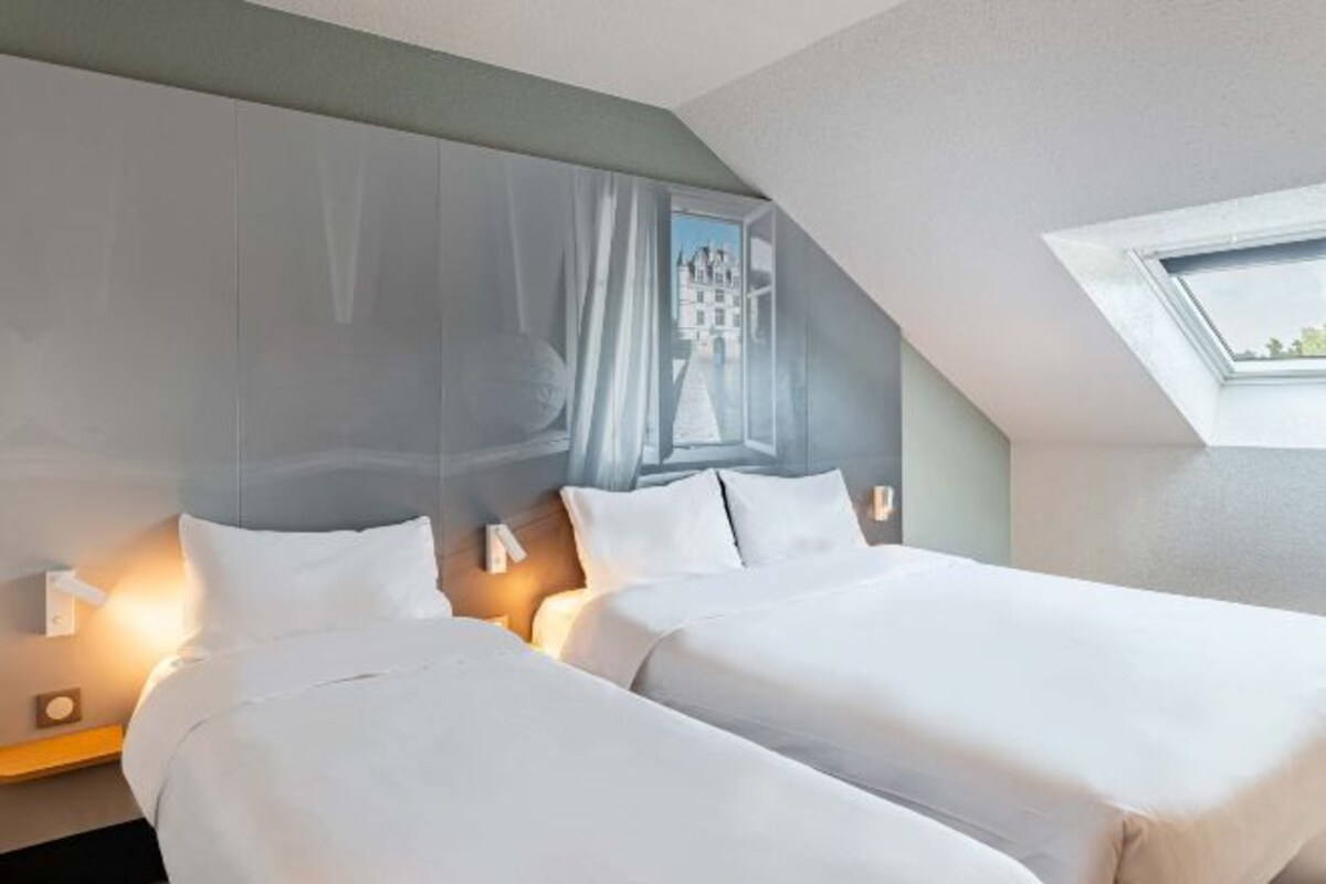 Habitación de hotel con dos camas, un ventanal con vistas y un tragaluz.