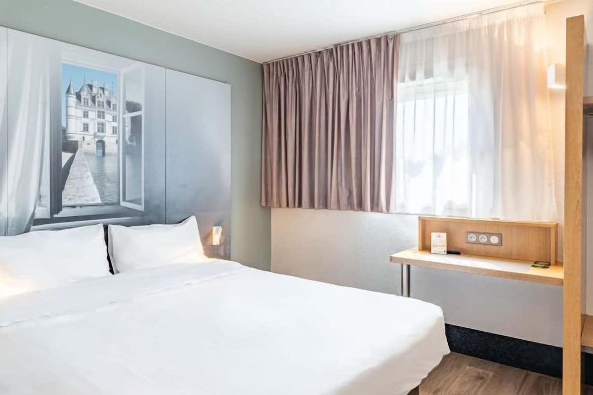 Habitación de hotel con una cama grande, una mesita de noche, una ventana con cortinas y un panel de control en la pared.