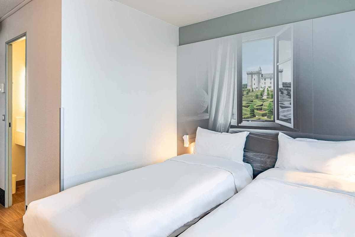 A hotel room with two beds, a large window with a view of a castle, and a door leading to a bathroom.