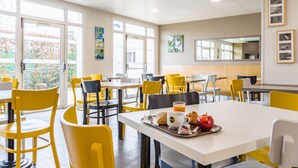 A bright cafeteria with yellow chairs and tables, featuring breakfast items like croissants and apples. - B&B HOTEL Tours Parc Expo St Avertin (Saint-Avertin)