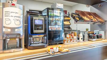 Een ontbijtbuffet met een koffieapparaat, een koelkast en een presentatie van gebak.