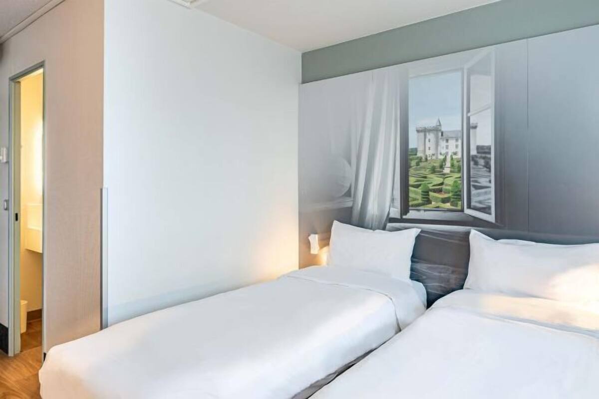 A hotel room with two beds, a window with a view, and a door leading to another room.