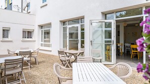 An outdoor patio area with white tables and chairs, a gravel floor, and a building entrance with glass doors. - B&B HOTEL Tours Parc Expo St Avertin (Saint-Avertin)