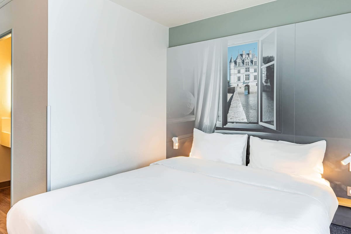 A hotel room with a large bed, a view of a historic building through an open window, and a modern design.