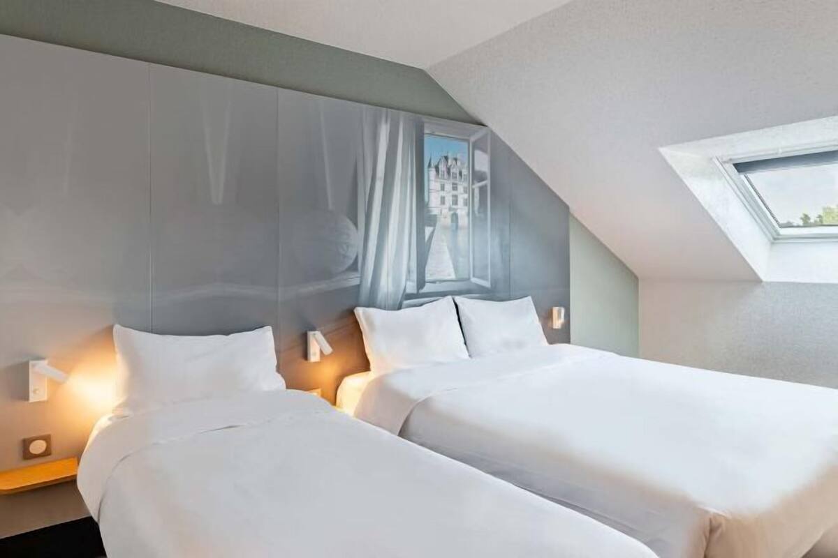 A hotel room with two beds, a large window with a view, and a skylight.