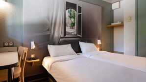 Een hotelkamer met een bed, nachtkastje, stoel en een muurschildering van een raam met gordijnen.