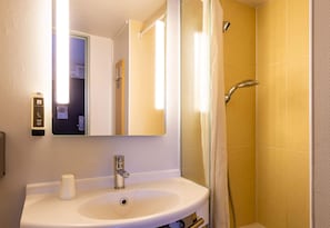 A bathroom with a white sink, a mirror, a shower with a glass door, and a towel rack. - B&B HOTEL Valence Nord (Bourg-les-Valence)