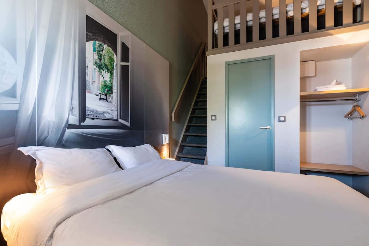 A bedroom with a bed, a window with curtains, a staircase, and a closet with hanging space.