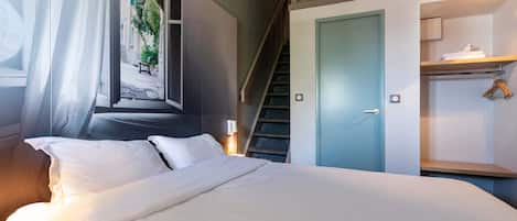 A bedroom with a bed, a window with curtains, a staircase, and a closet with hanging space.