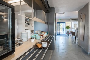 A modern kitchen area with a buffet setup, including trays with food and utensils. - B&B HOTEL Valence Nord (Bourg-les-Valence)
