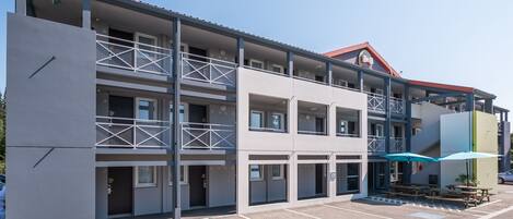 Un hotel de varios pisos con balcones, estacionamiento y mesas al aire libre.