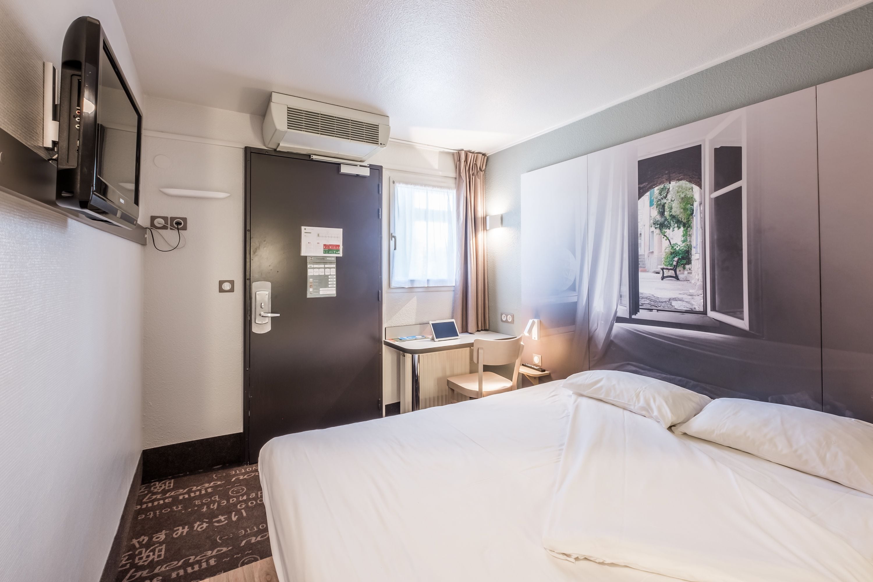 Une chambre d’hôtel équipée d’un lit, d’un bureau avec un ordinateur portable, d’une télévision et d’un appareil de climatisation.