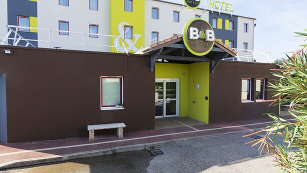 A B&B hotel with a modern design, featuring a prominent logo, a staircase leading to the entrance, and a bench outside. - B&B HOTEL Valence Sud (Valence)