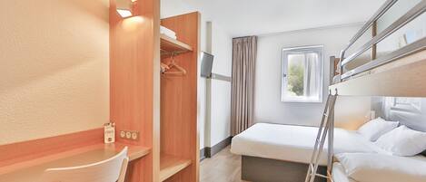 Quarto de hotel compacto com beliche, escrivaninha com cadeira, guarda-roupa e janela com cortinas.