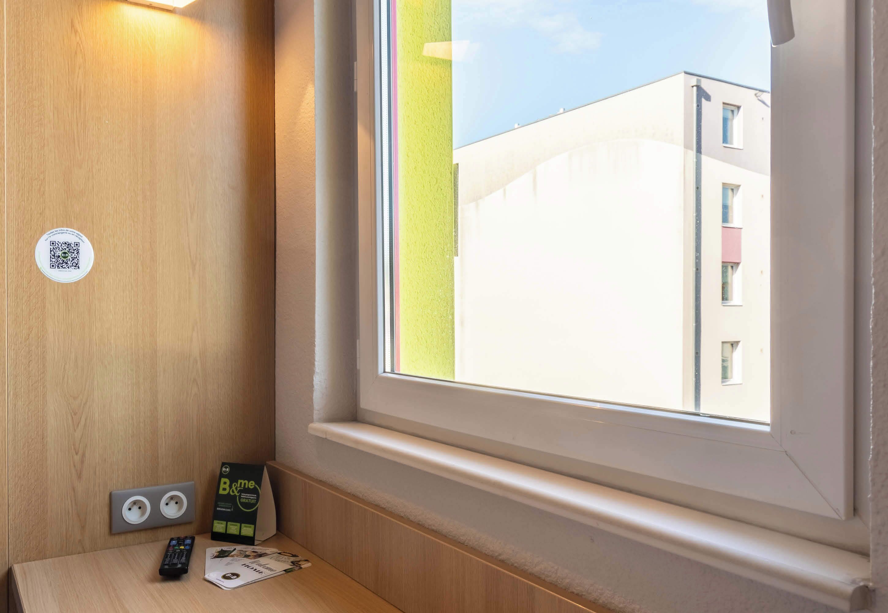 Una habitación de hotel con ventana, pared de madera, un código QR, un letrero de B&Q y un control remoto.